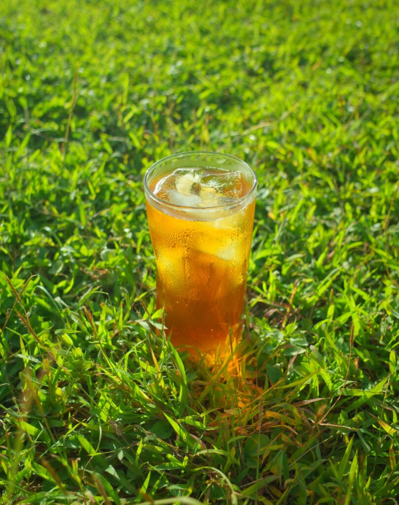 A glass of Tropic Gold iced tea standing in green grass